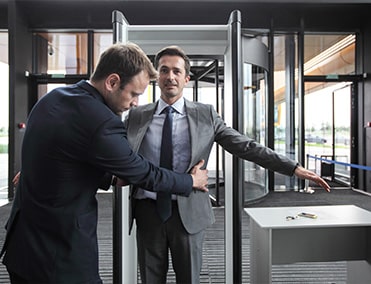 a man in a suit stands with arms and legs spread as a security officer pats him down at an airport terminal